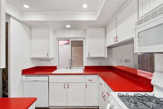 kitchen with white appliances, crown molding, sink, a tray ceiling, and white cabinetry