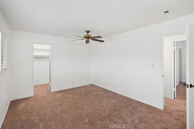 unfurnished bedroom with a closet, a walk in closet, light colored carpet, and ceiling fan