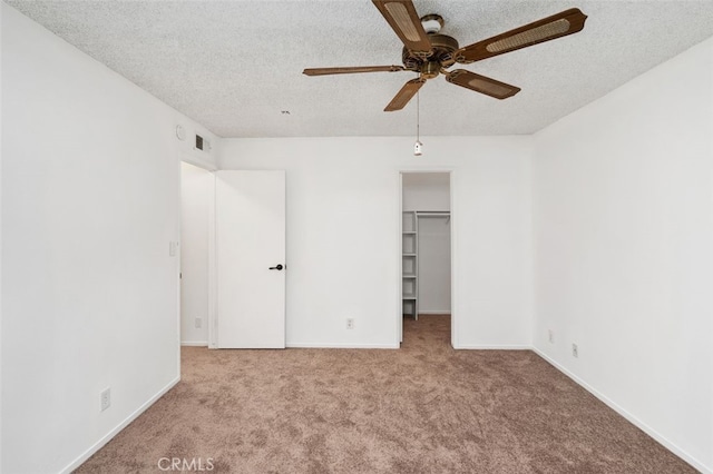 unfurnished bedroom with ceiling fan, a textured ceiling, a walk in closet, light carpet, and a closet