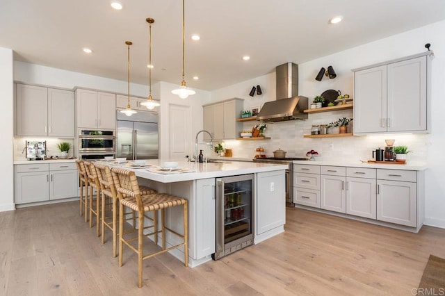 kitchen featuring sink, wine cooler, high end appliances, a center island with sink, and wall chimney exhaust hood