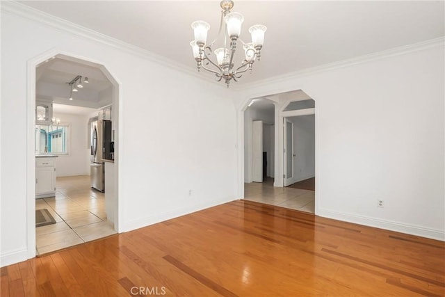 unfurnished room featuring light wood-type flooring, track lighting, ornamental molding, and a notable chandelier