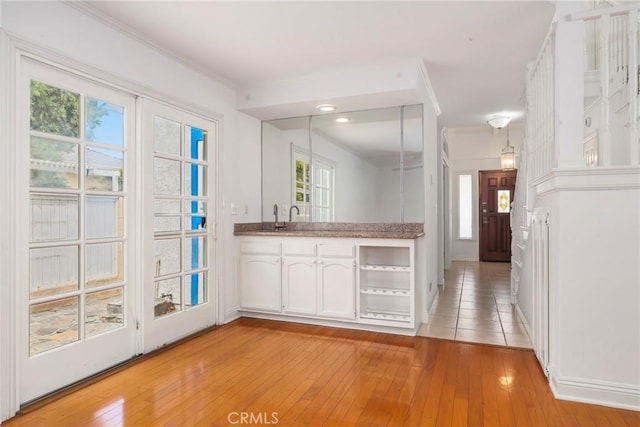 kitchen with kitchen peninsula, crown molding, white cabinets, and light hardwood / wood-style floors