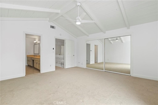 unfurnished bedroom with ensuite bathroom, light colored carpet, ceiling fan, vaulted ceiling with beams, and a closet