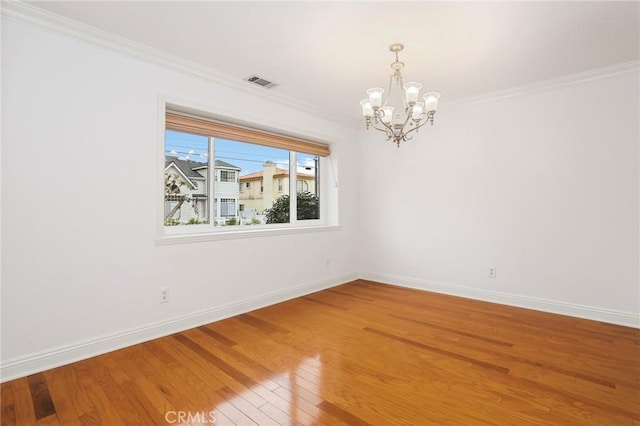 spare room featuring wood-type flooring, crown molding, and a notable chandelier