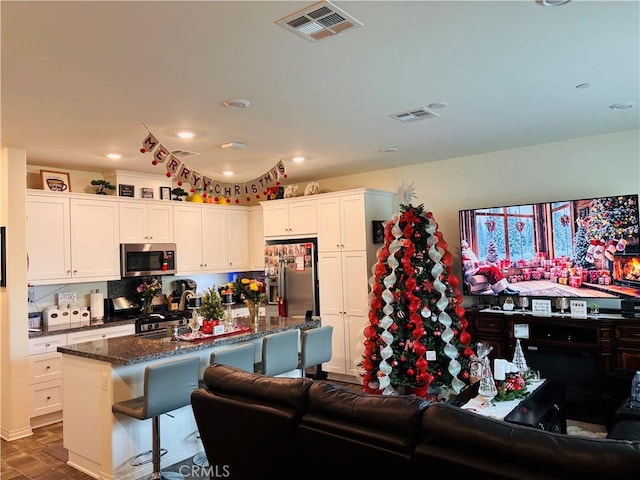 kitchen featuring a kitchen breakfast bar, dark stone counters, stainless steel appliances, a center island with sink, and white cabinetry