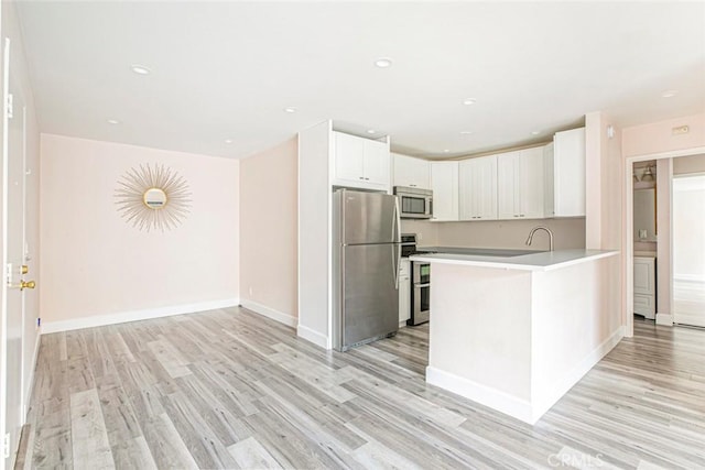 kitchen featuring white cabinets, appliances with stainless steel finishes, light hardwood / wood-style floors, and kitchen peninsula