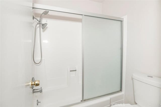 bathroom featuring combined bath / shower with glass door and toilet