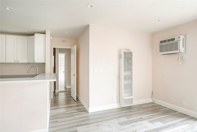 kitchen with white cabinets, light hardwood / wood-style flooring, and a wall unit AC