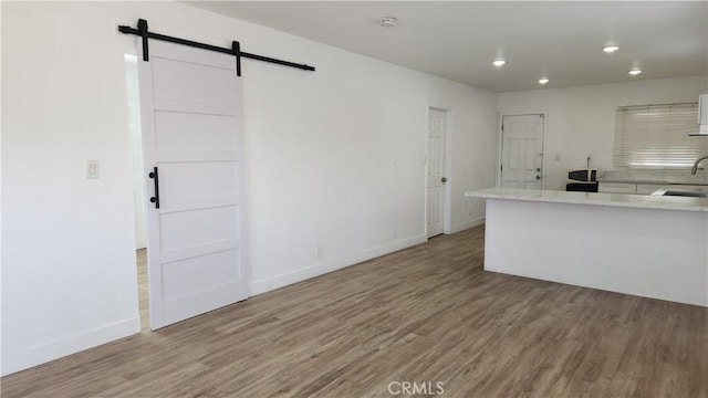 kitchen with hardwood / wood-style flooring, a barn door, sink, and white cabinets