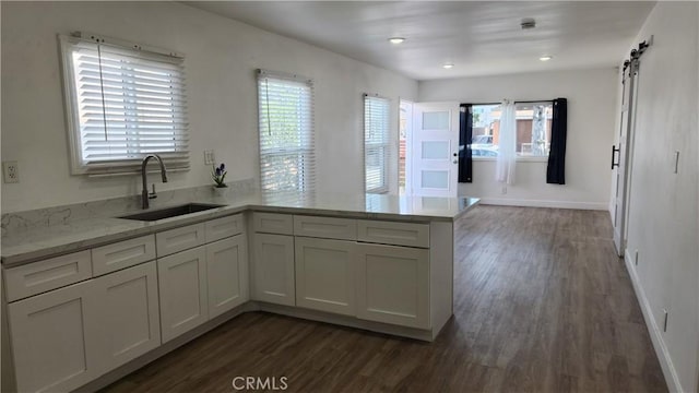 kitchen with a barn door, sink, dark hardwood / wood-style floors, and kitchen peninsula