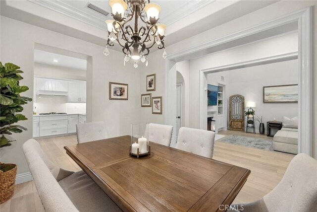 dining room featuring crown molding, a notable chandelier, a tray ceiling, and light hardwood / wood-style flooring