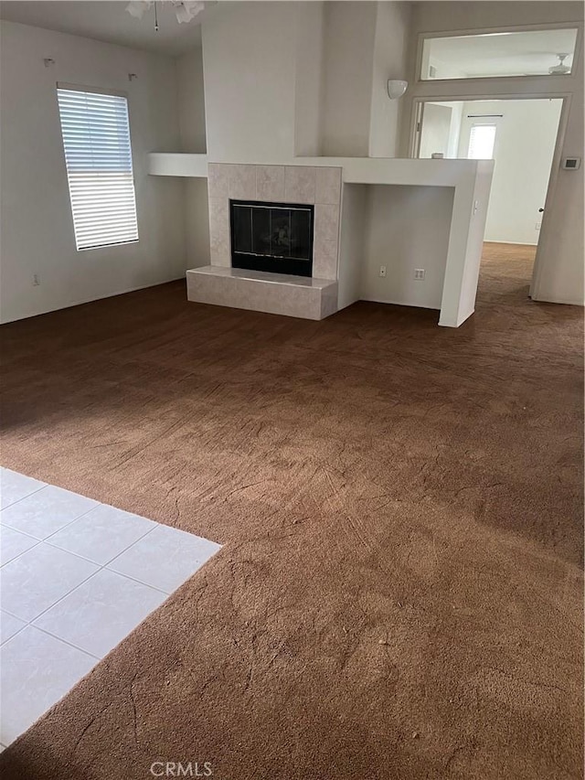 unfurnished living room with ceiling fan, plenty of natural light, a tile fireplace, and carpet flooring