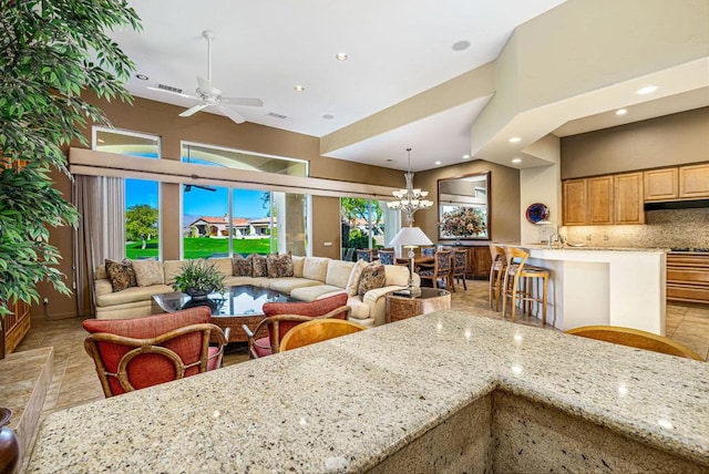 kitchen featuring backsplash, ceiling fan with notable chandelier, hanging light fixtures, light stone countertops, and a kitchen bar