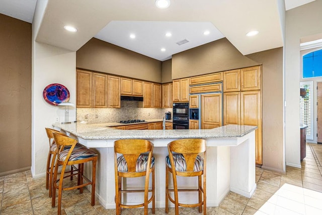 kitchen featuring black appliances, a breakfast bar, light stone countertops, and kitchen peninsula