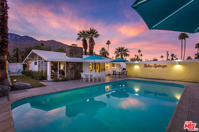 pool at dusk featuring a mountain view and a patio