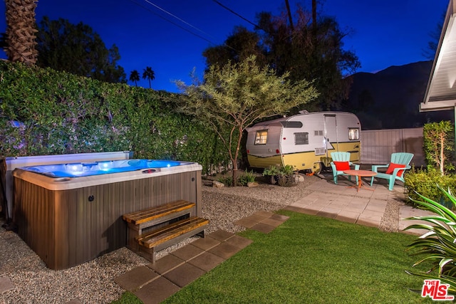 yard at night featuring a mountain view, a patio, and a hot tub