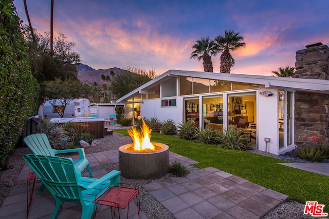 patio terrace at dusk with a mountain view, a hot tub, and a fire pit