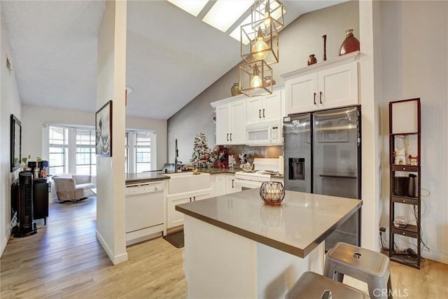 kitchen with light hardwood / wood-style flooring, kitchen peninsula, decorative light fixtures, white appliances, and a breakfast bar area