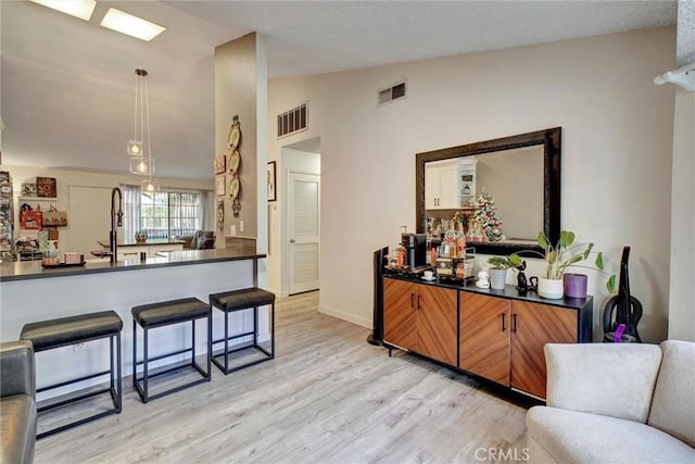 kitchen featuring pendant lighting, sink, vaulted ceiling, light hardwood / wood-style floors, and a breakfast bar area