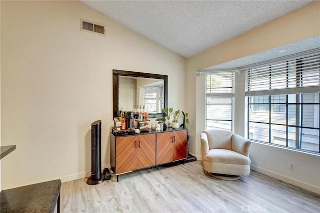 living area featuring a textured ceiling, light hardwood / wood-style flooring, and vaulted ceiling