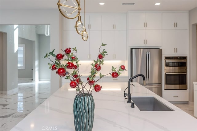 kitchen with light stone countertops, stainless steel appliances, sink, pendant lighting, and white cabinetry