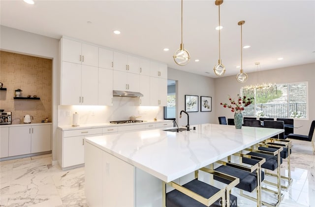 kitchen featuring a spacious island, white cabinetry, sink, and hanging light fixtures