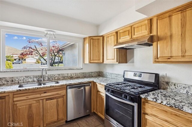 kitchen with dark tile patterned flooring, light stone countertops, sink, and stainless steel appliances