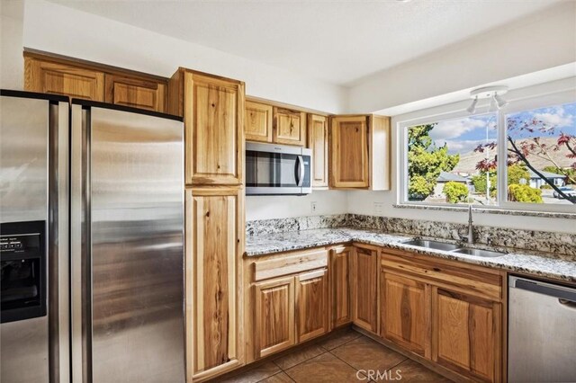 kitchen with dark tile patterned floors, stainless steel appliances, light stone counters, and sink