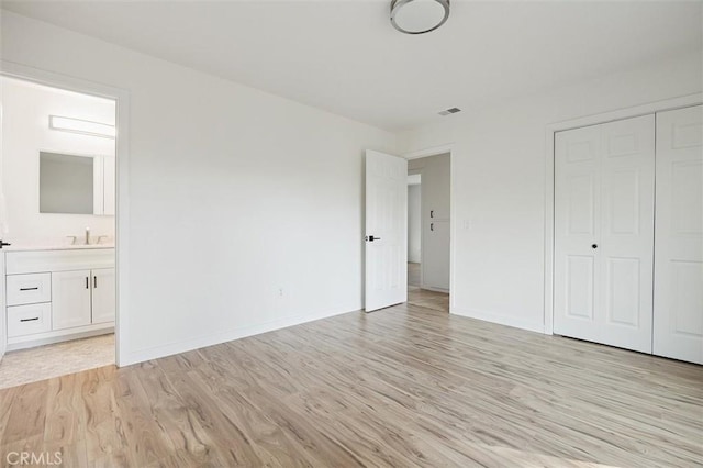 unfurnished bedroom featuring ensuite bath, a closet, sink, and light hardwood / wood-style floors