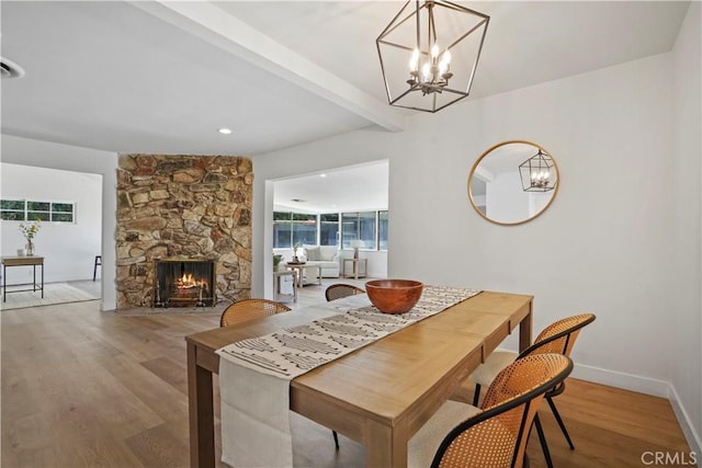 dining space featuring hardwood / wood-style floors, beam ceiling, a chandelier, and a fireplace