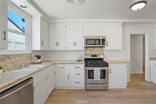 kitchen with appliances with stainless steel finishes, light hardwood / wood-style flooring, white cabinets, and backsplash