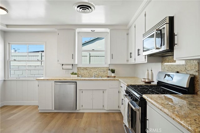 kitchen with plenty of natural light, appliances with stainless steel finishes, light hardwood / wood-style flooring, and white cabinets