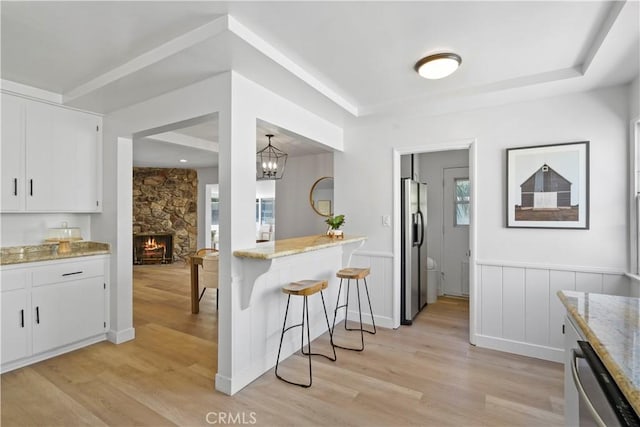 kitchen with pendant lighting, white cabinetry, stainless steel appliances, a stone fireplace, and light stone counters