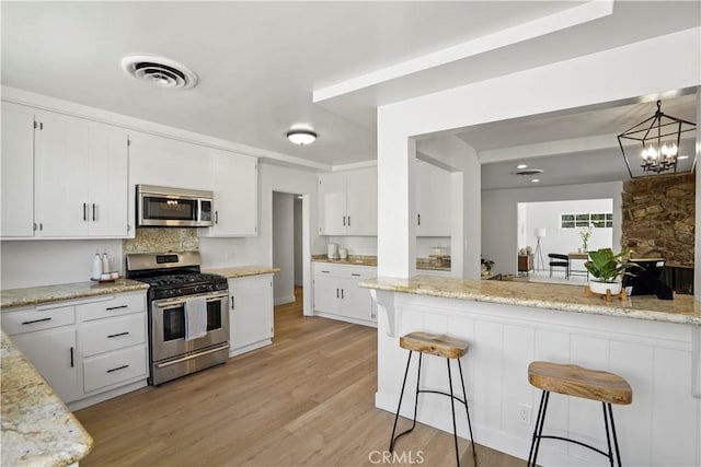 kitchen featuring light stone countertops, white cabinets, appliances with stainless steel finishes, light hardwood / wood-style floors, and a breakfast bar area