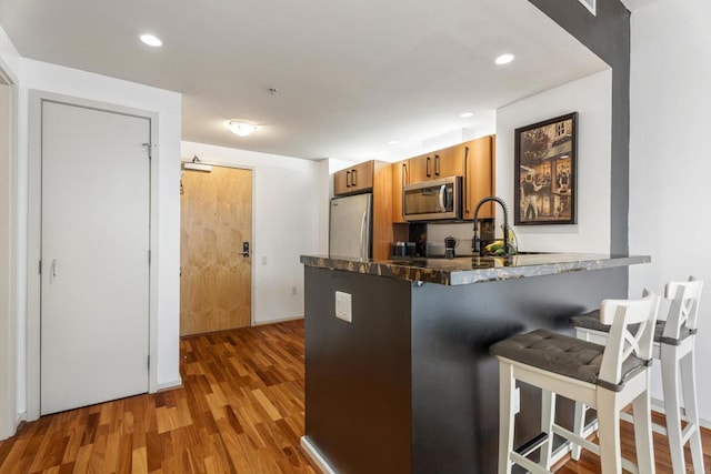 kitchen with sink, stainless steel appliances, kitchen peninsula, light hardwood / wood-style floors, and a breakfast bar