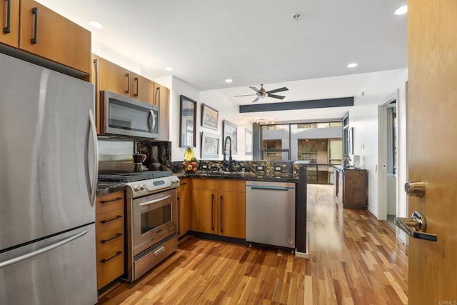 kitchen with kitchen peninsula, tasteful backsplash, stainless steel appliances, sink, and light hardwood / wood-style floors