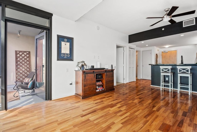 interior space featuring hardwood / wood-style floors, ceiling fan, a kitchen breakfast bar, and dark stone counters