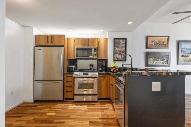 kitchen with kitchen peninsula, appliances with stainless steel finishes, sink, dark stone countertops, and light hardwood / wood-style floors