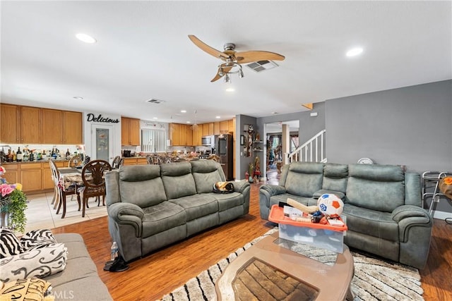 living room featuring a ceiling fan, recessed lighting, light wood-style flooring, and stairs