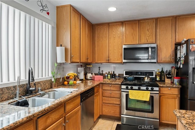 kitchen featuring light stone countertops, appliances with stainless steel finishes, brown cabinets, and a sink