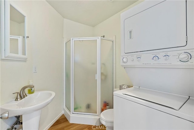 bathroom featuring an enclosed shower, sink, wood-type flooring, stacked washer and dryer, and toilet