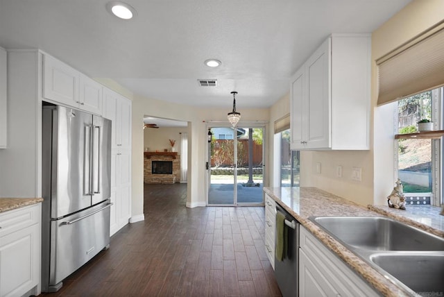 kitchen with white cabinetry, dark wood-type flooring, stainless steel appliances, a stone fireplace, and decorative light fixtures