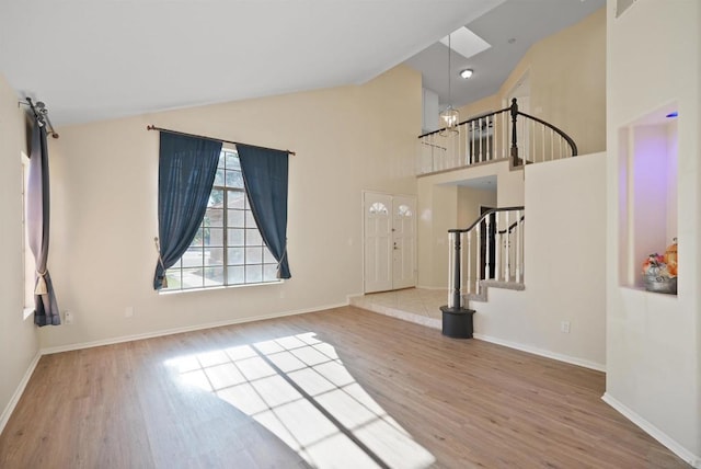 unfurnished living room featuring light wood-type flooring, high vaulted ceiling, and a notable chandelier