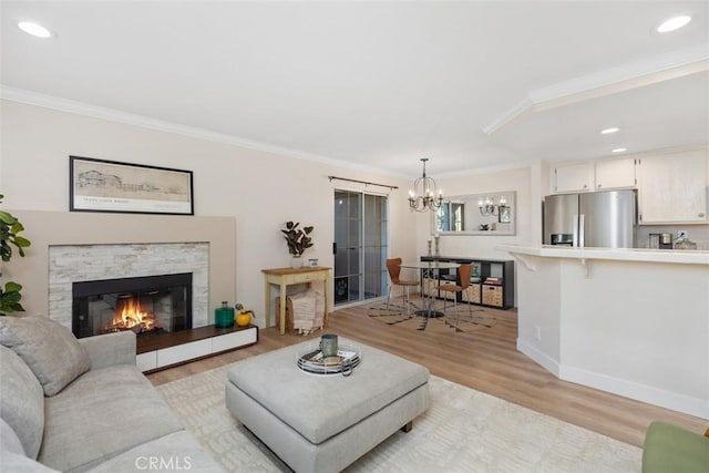 living room with light hardwood / wood-style floors, crown molding, a stone fireplace, and an inviting chandelier