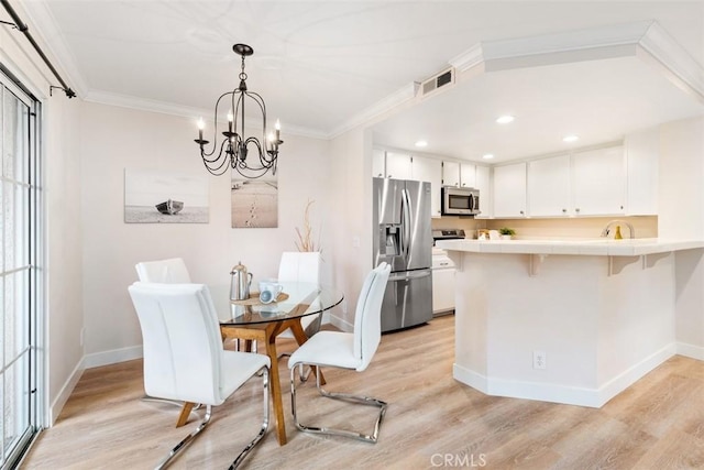 dining area with crown molding, light hardwood / wood-style floors, and an inviting chandelier