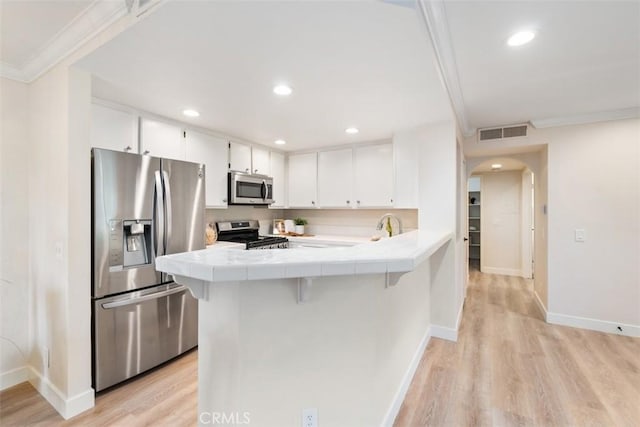 kitchen with light hardwood / wood-style flooring, white cabinetry, tile countertops, ornamental molding, and stainless steel appliances