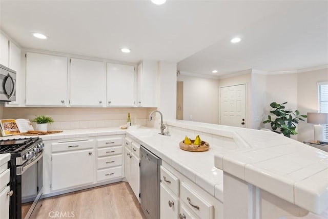 kitchen with sink, white cabinetry, tile counters, and appliances with stainless steel finishes