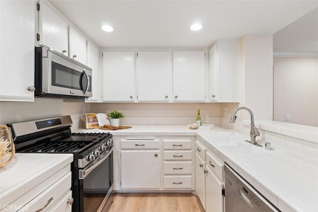 kitchen with white cabinets, appliances with stainless steel finishes, sink, and tile countertops