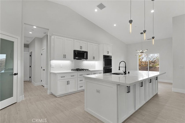 kitchen featuring white cabinets, pendant lighting, an island with sink, and black appliances