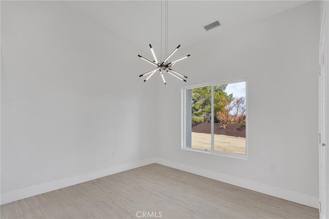 empty room featuring light wood-type flooring, an inviting chandelier, and vaulted ceiling